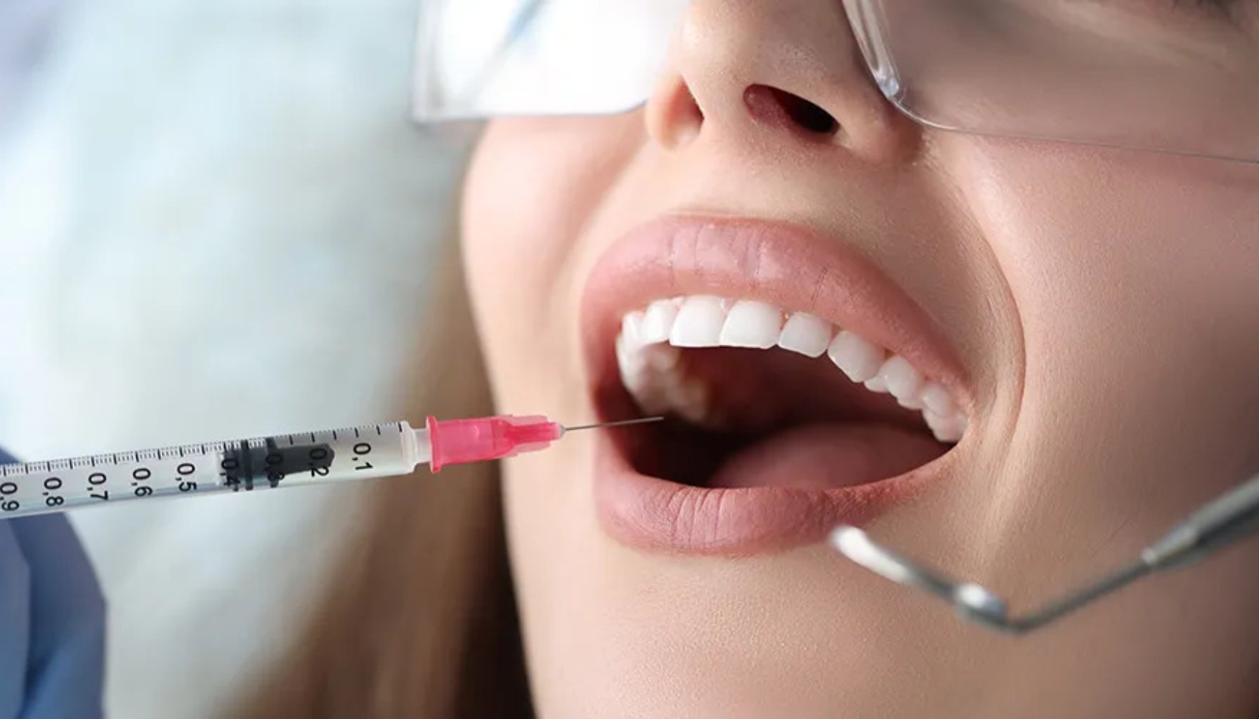 En pasient med beskyttelsesbriller får en bedøvelsesprøyte i munnen hos tannlegen før en tannbehandling.