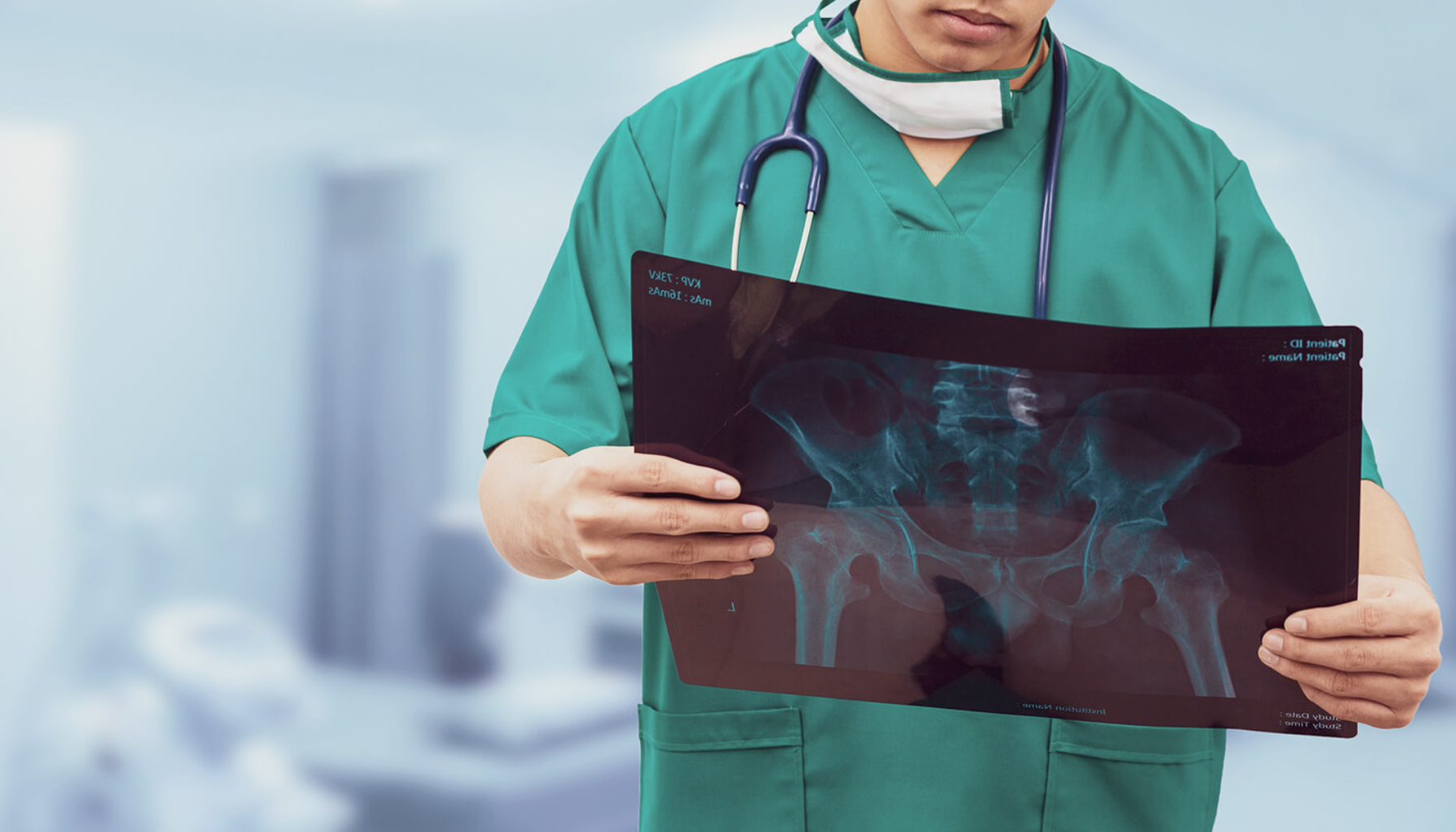 En lege i grønne kirurgiske klær og stetoskop analyserer en røntgenbilde av bekkenet i et medisinsk undersøkelsesrom.