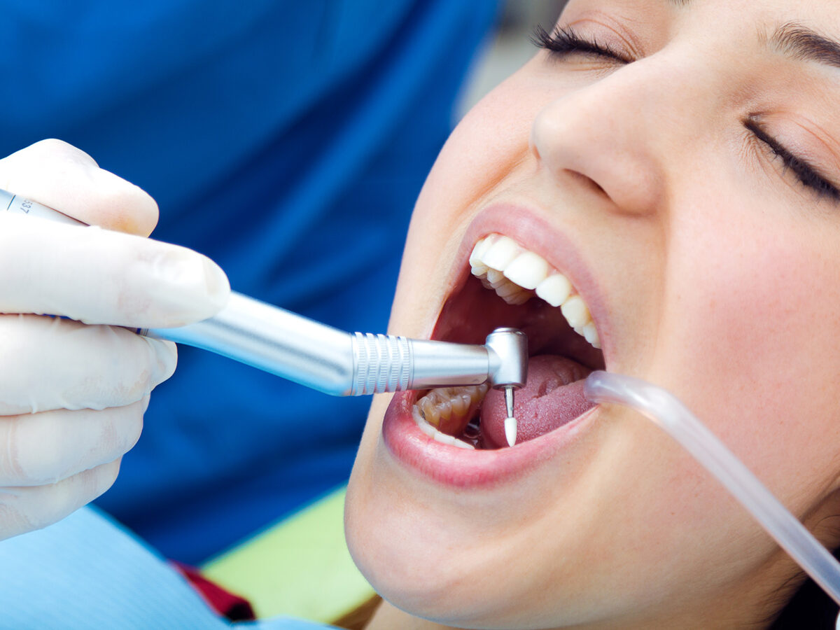 En tannlege bruker en dental drill på en pasient under en behandling for å rense tennene hennes.