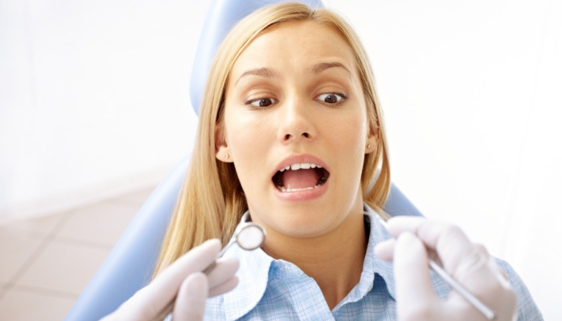 Kvinne i tannlegestol ser nervøs ut mens tannlegen holder tanninstrumenter foran henne under undersøkelse.