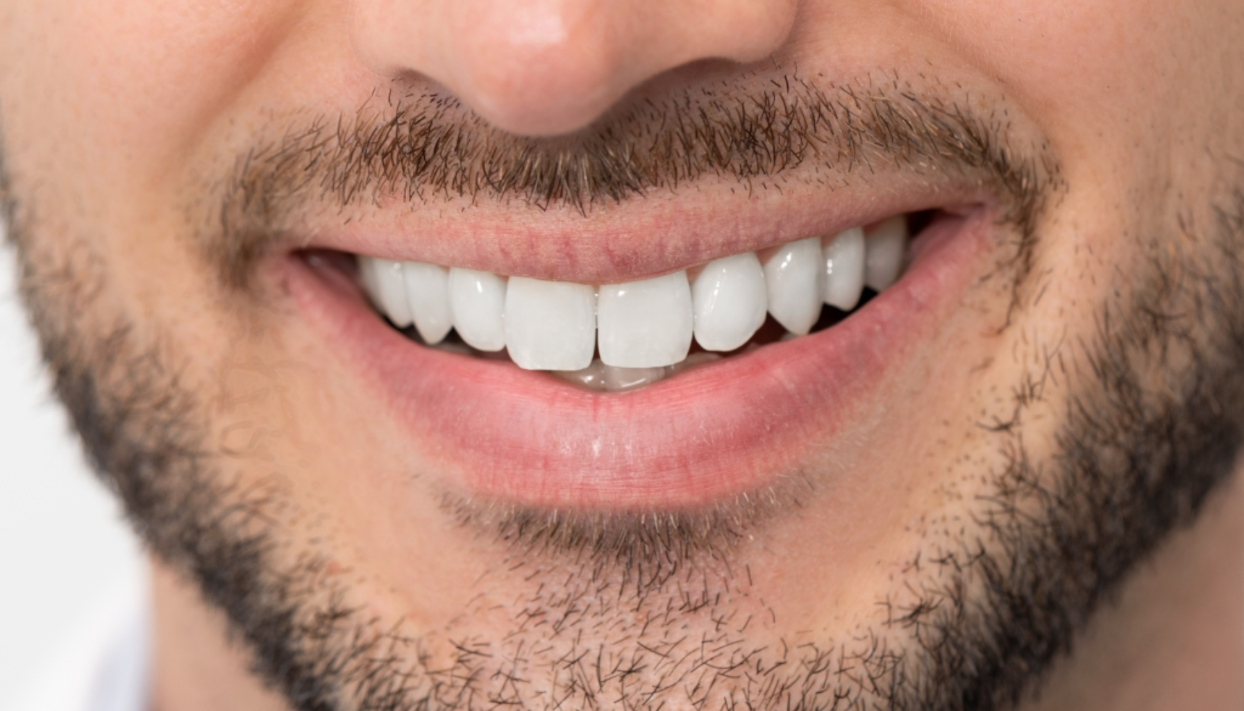 Et nærbilde av en smilende mann med skjegg og perfekte, hvite tenner som viser god tannhelse og estetisk tannbehandling. hvert tannresorpsjon tr forl får veterinæren